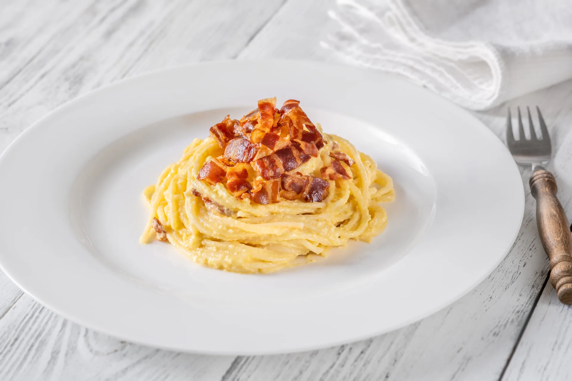Piatto di spaghetti alla carbonara con crema liscia e lucida che avvolge la pasta, con guanciale croccante sopra