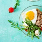 Piatto con uovo all'occhio di bue, cereali, rucola, feta e pomodorini