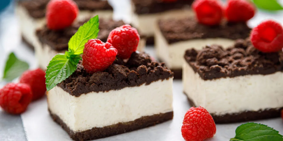 Quadrotti di cheesecake con base al cacao, crema bianca e lamponi