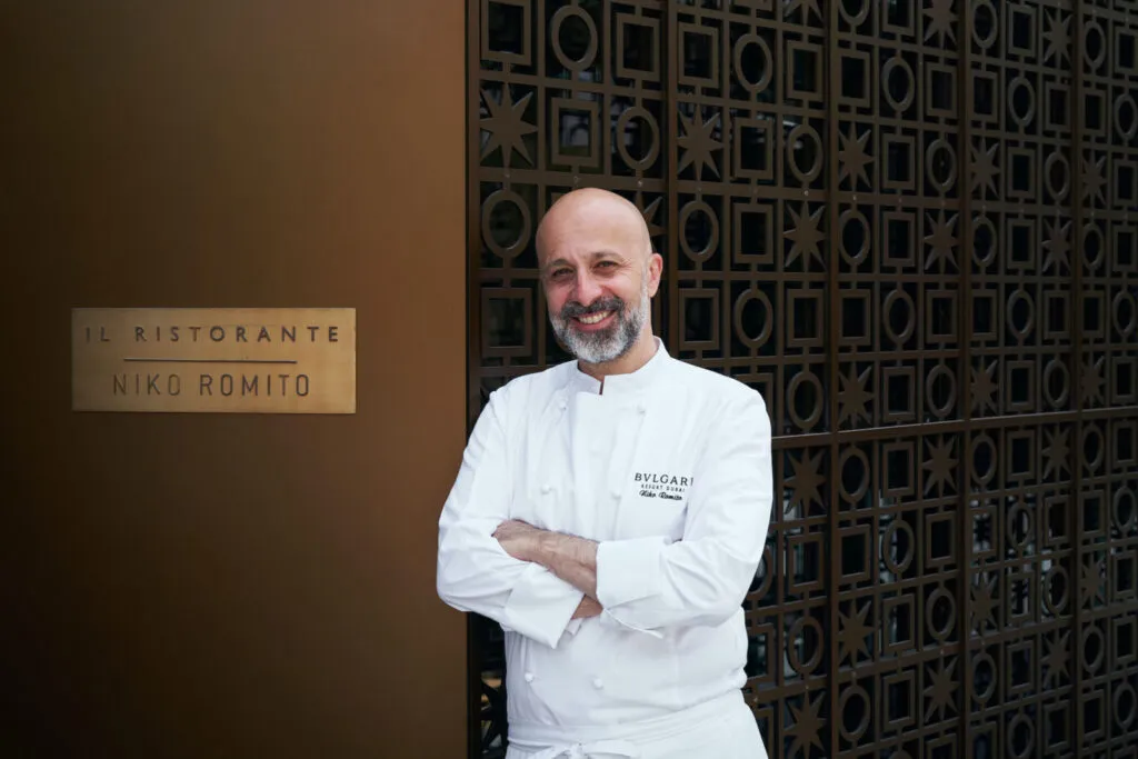 Lo chef Niko Romito in giacca bianca, a braccia conserte, accanto alla targa in ottone del suo ristorante