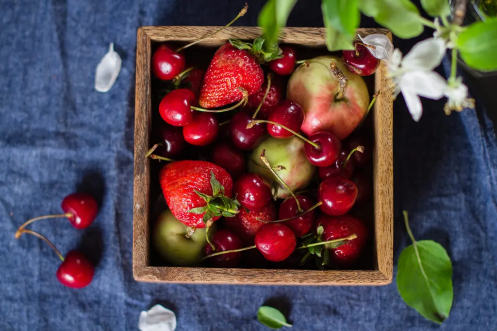 Cassetta di legno con fragole, ciliegie e mele fresche
