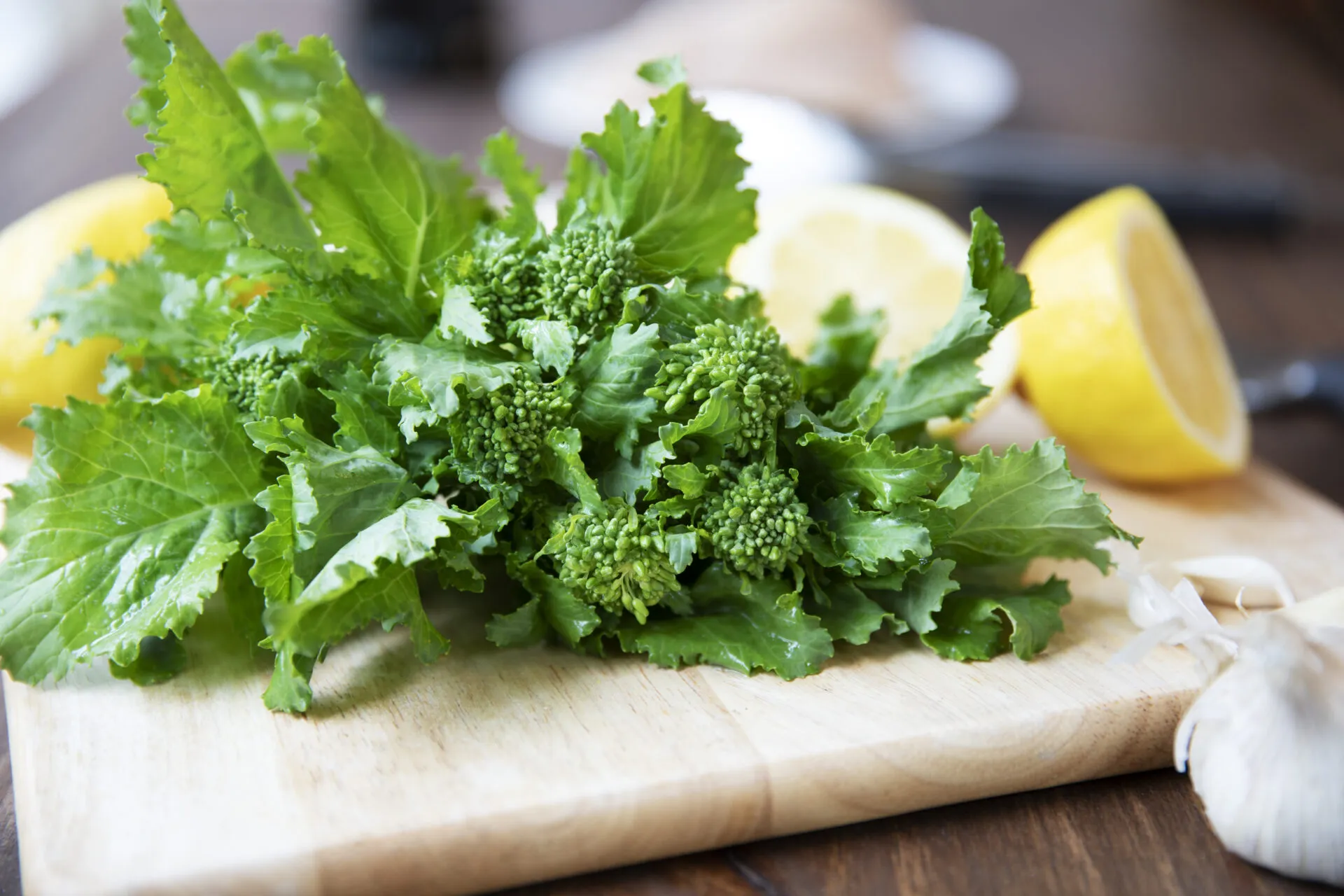 Mazzo di cime di rapa fresche con foglie intere e cimette su un tagliere di legno, accanto ad aglio e limone