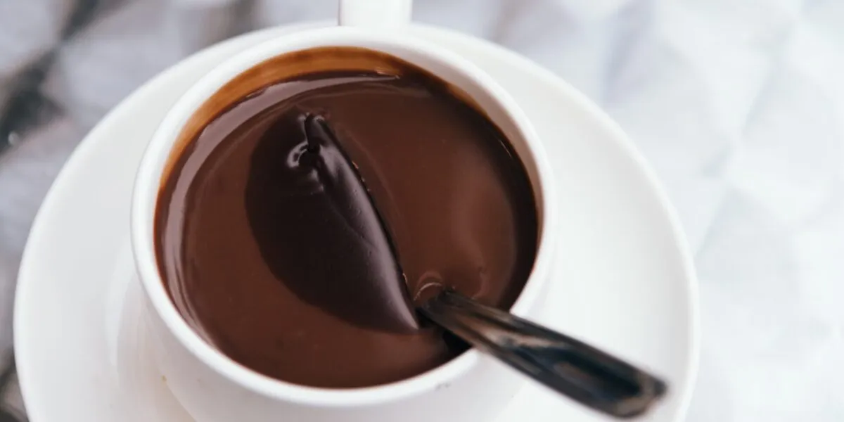 Cioccolata calda densa in tazza bianca con il cucchiaino