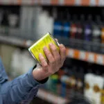 Mano che gira una scatoletta per leggere l'etichetta con la data, davanti allo scaffale di un supermercato