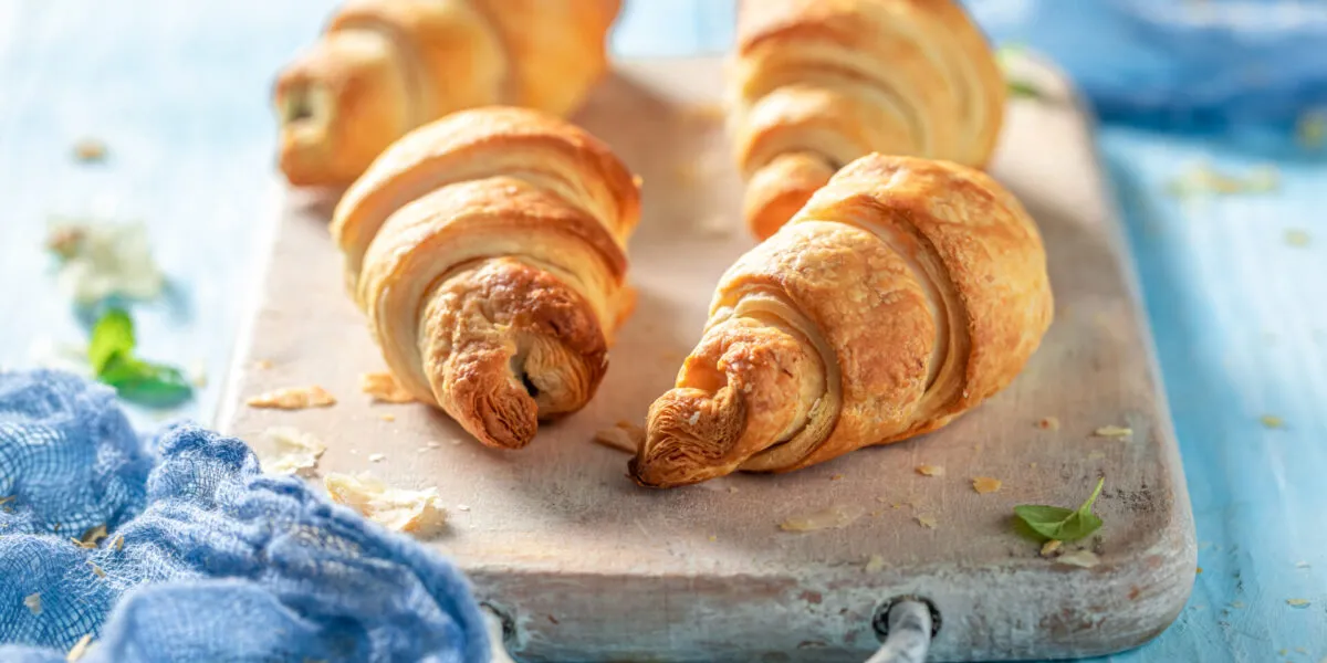 Cornetti di pasta sfoglia dorati su un tagliere di legno chiaro