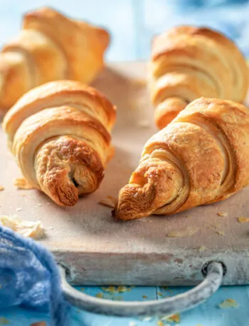 Cornetti di pasta sfoglia dorati su un tagliere di legno chiaro