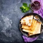 Crêpes piegate su un piatto scuro con confettura di frutti rossi