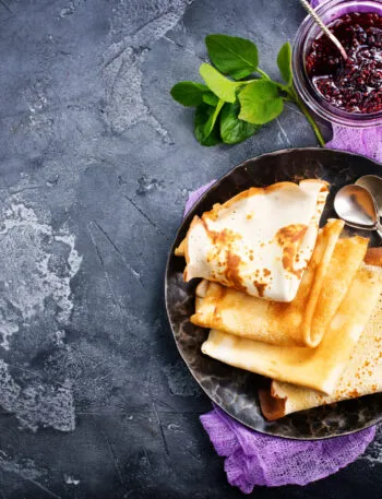 Crêpes piegate su un piatto scuro con confettura di frutti rossi