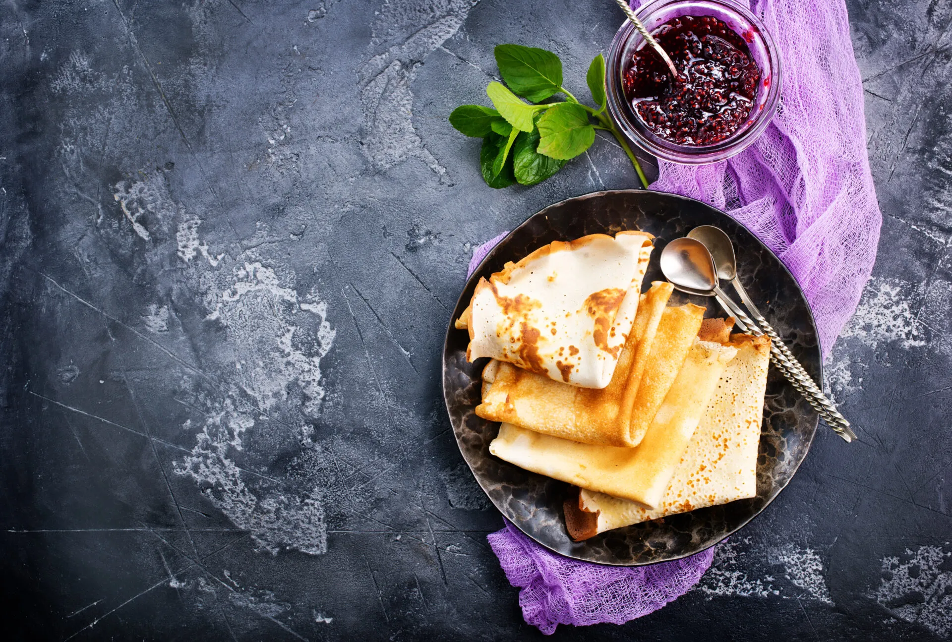 Crêpes piegate su un piatto scuro con confettura di frutti rossi