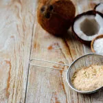 Farina di cocco in un colino accanto a cocco rapè e noci di cocco