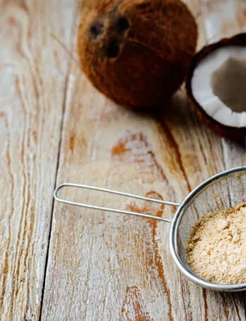 Farina di cocco in un colino accanto a cocco rapè e noci di cocco