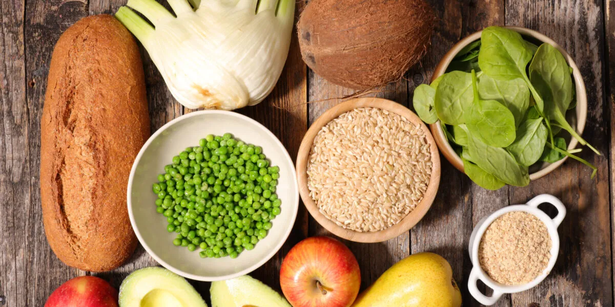Vista dall’alto di alimenti ricchi di fibre su un tavolo di legno: pane integrale, finocchio, piselli, riso integrale, spinaci, avena, mele, pera e avocado