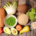 Vista dall’alto di alimenti ricchi di fibre su un tavolo di legno: pane integrale, finocchio, piselli, riso integrale, spinaci, avena, mele, pera e avocado