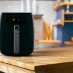 Friggitrice ad aria nera appoggiata su un piano di lavoro in legno chiaro, con il display acceso che segna 180 gradi