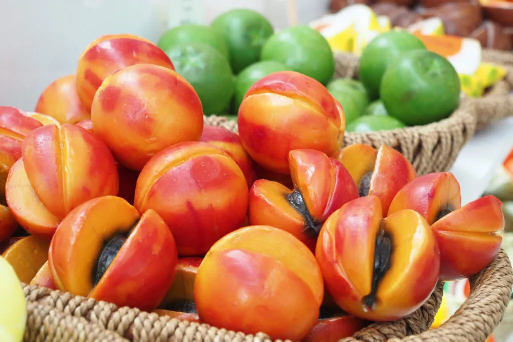 Cesti di vimini pieni di frutta martorana modellata a forma di pesche e albicocche, alcune tagliate a metà, in una pasticceria siciliana