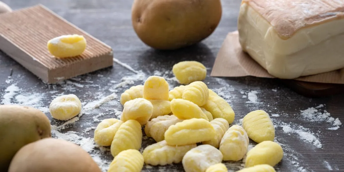 Gnocchi di patate crudi rigati su un piano di legno infarinato, con patate intere e un rigagnocchi di legno accanto