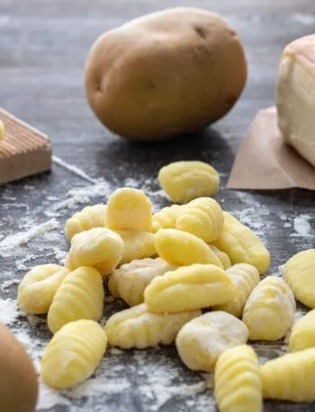 Gnocchi di patate crudi rigati su un piano di legno infarinato, con patate intere e un rigagnocchi di legno accanto