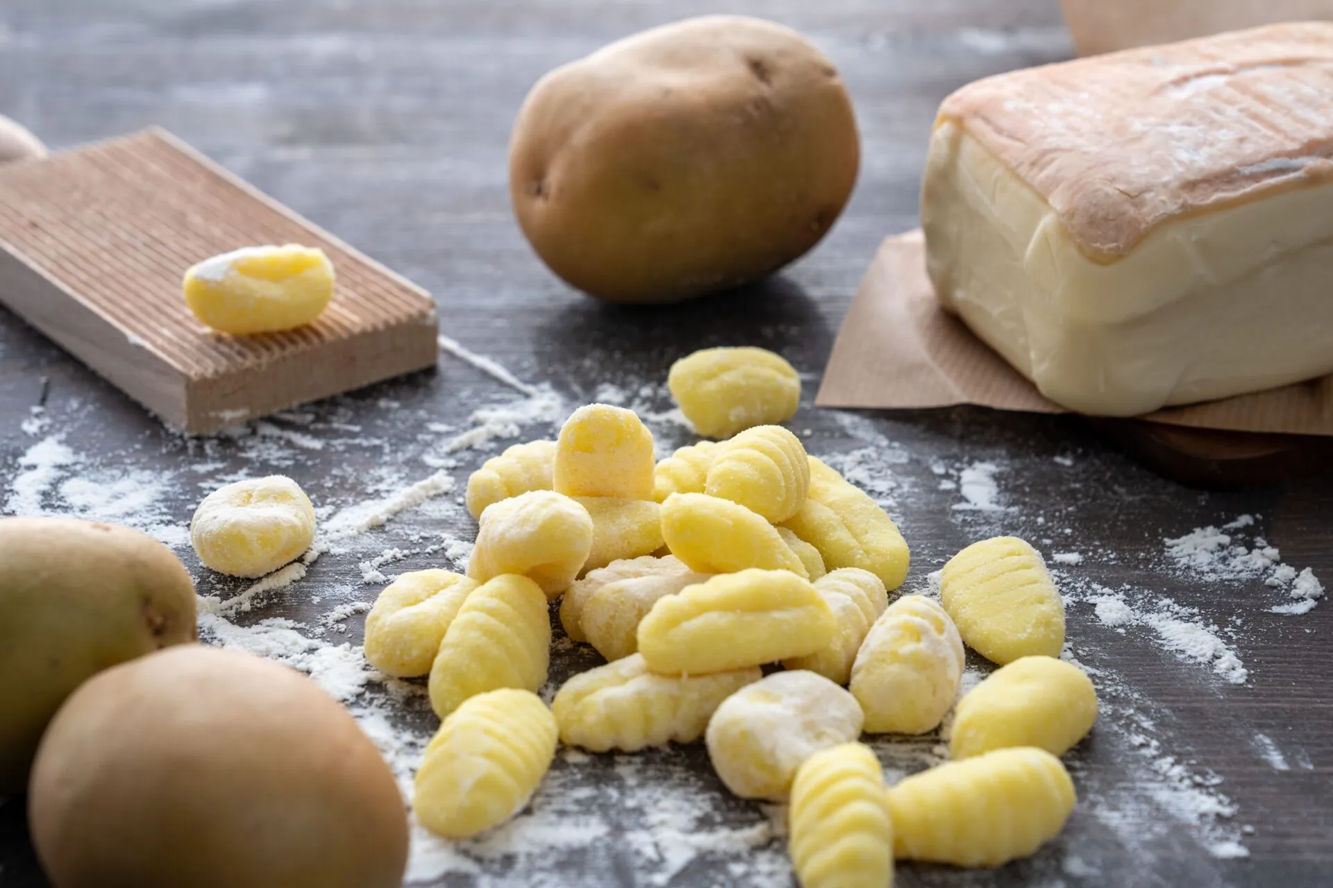 Gnocchi di patate crudi rigati su un piano di legno infarinato, con patate intere e un rigagnocchi di legno accanto