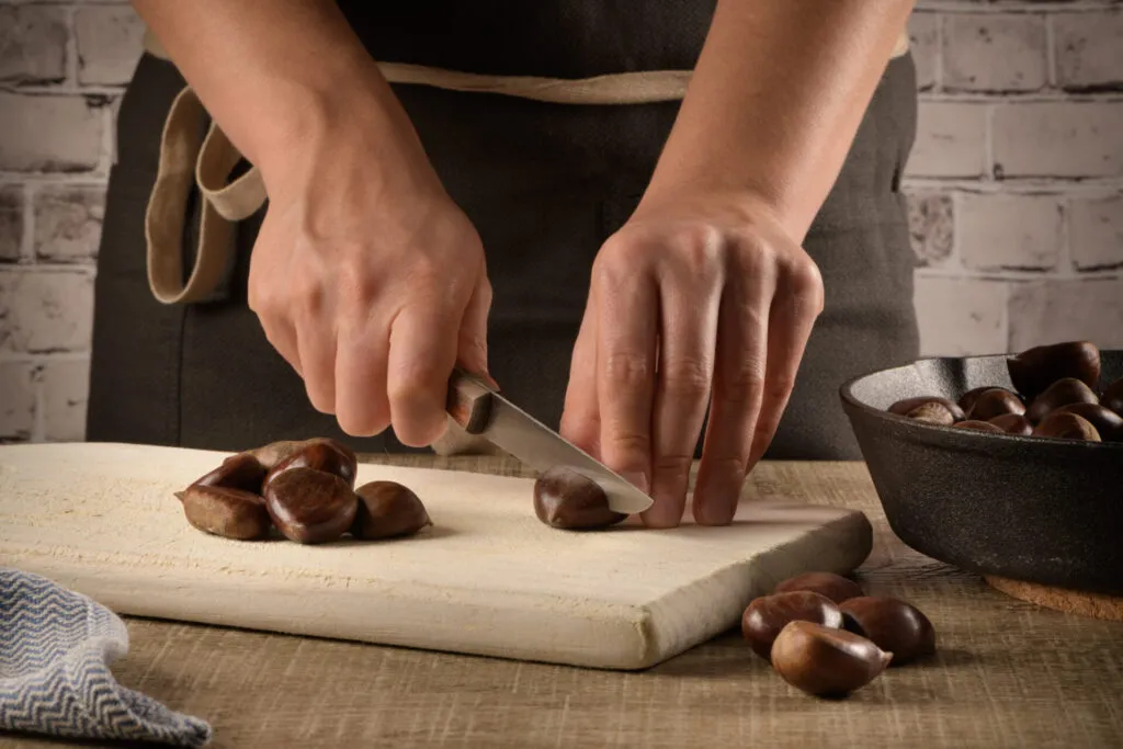 Mani che incidono la buccia di una castagna con un coltellino