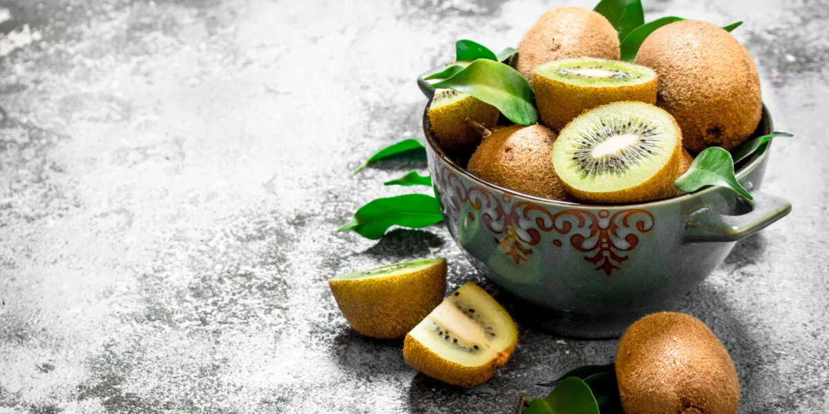 Ciotola di ceramica con kiwi interi e tagliati, due a polpa verde e due spicchi a polpa gialla, con foglie fresche