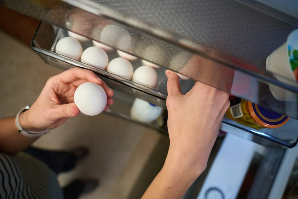 Mano che prende un uovo dal portauova nello sportello del frigo