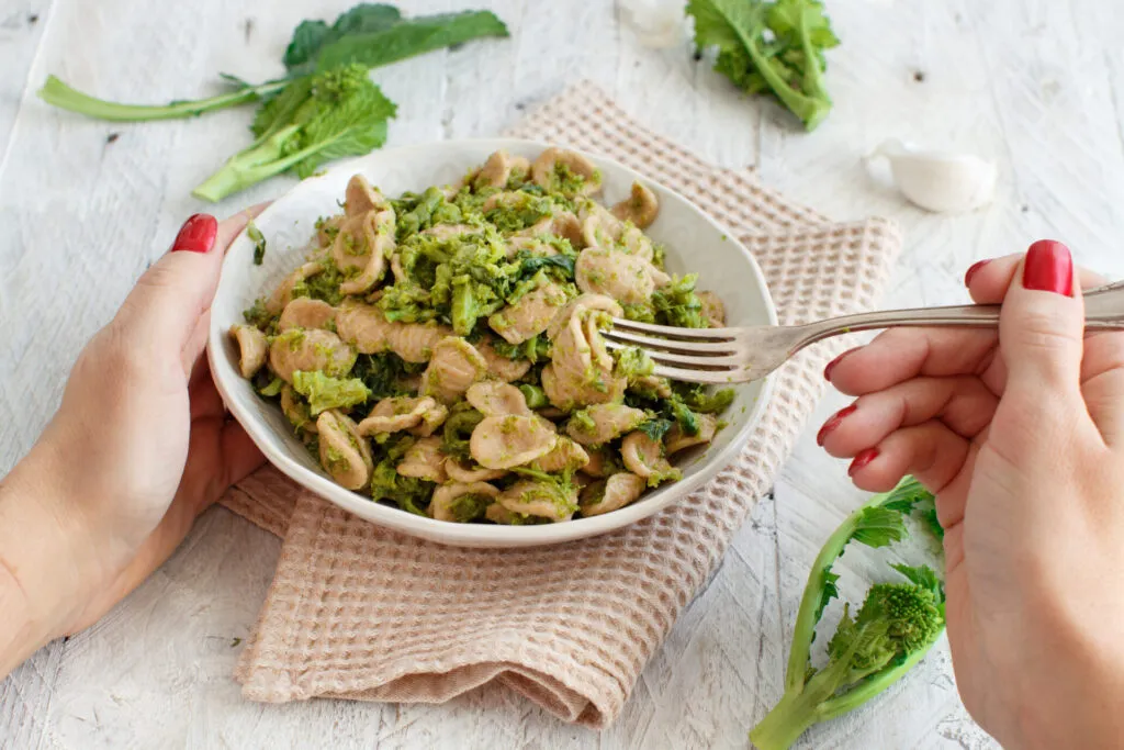 Piatto di orecchiette integrali con cime di rapa tenuto tra le mani, con foglie e cimette fresche accanto