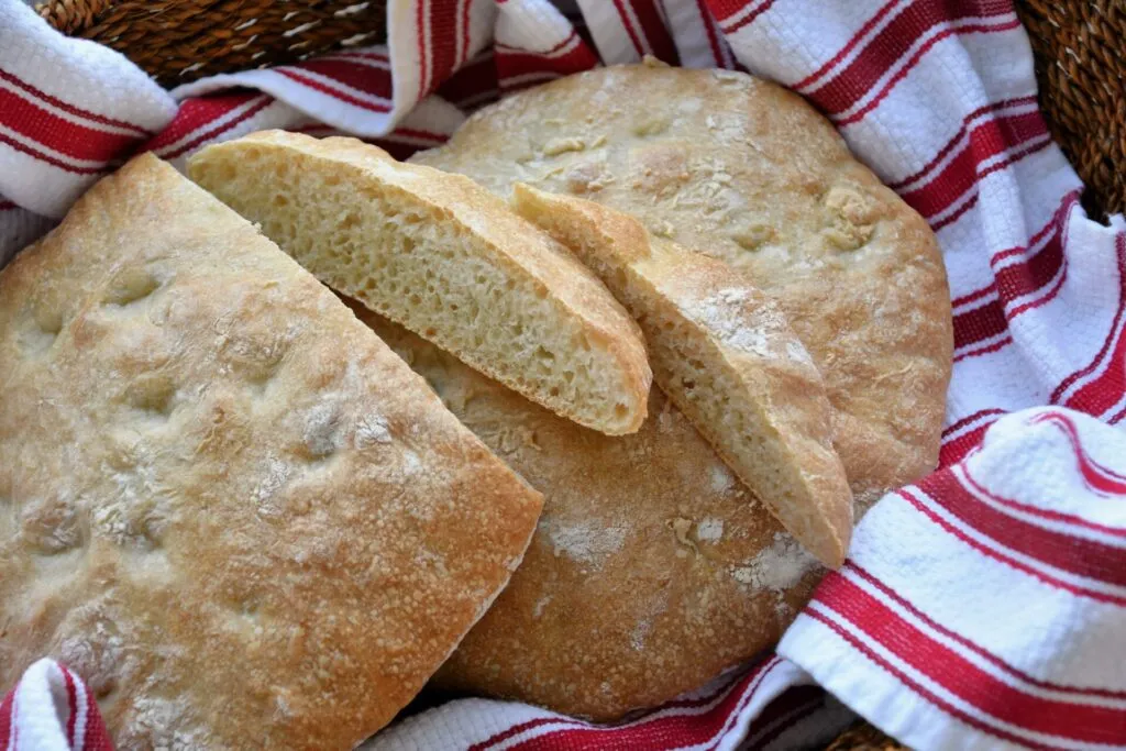 Pagnotta di pane chiaro e bassa, tagliata a fette, con la mollica fitta e gli alveoli piccoli, su un canovaccio a righe