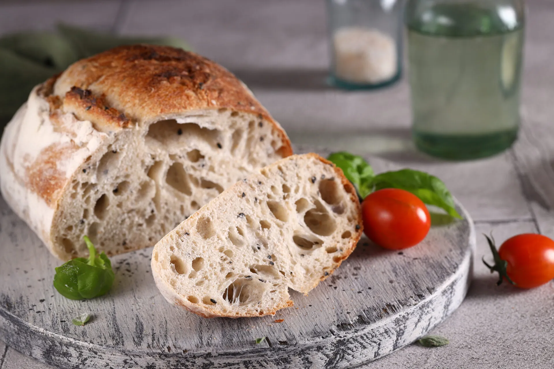 Pagnotta di pane a lievitazione naturale tagliata, con la mollica alveolata e la crosta dorata, su un tagliere di legno con pomodorini e basilico