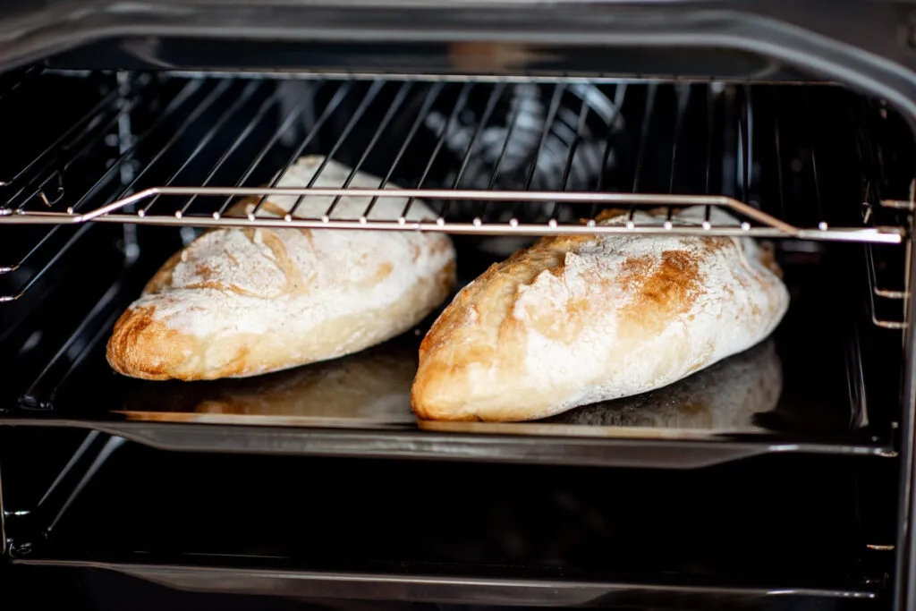 Due filoni di pane in cottura sulla teglia dentro un forno domestico, con la crosta che inizia a dorarsi