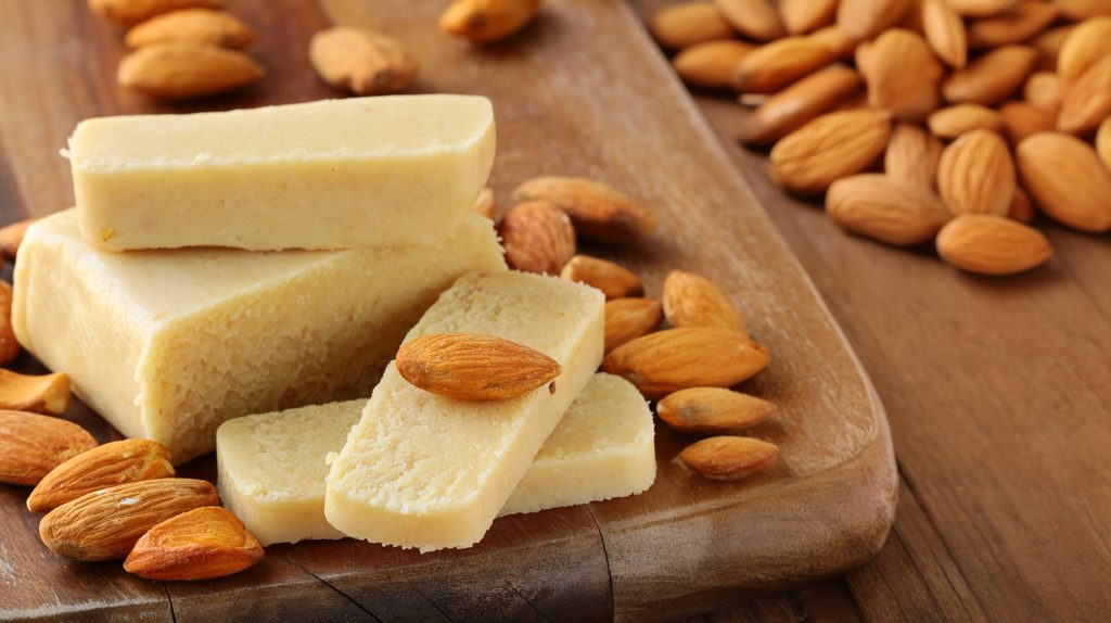 Panetti di pasta di mandorle tagliati, compatti e lisci, su un tagliere di legno circondati da mandorle intere