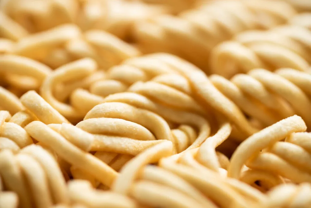Primo piano di fili di pasta fresca spessi e irregolari, infarinati, ammucchiati uno sull'altro