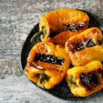 Peperoni gialli e arancioni arrostiti interi con la pelle raggrinzita e abbrustolita su un piatto scuro