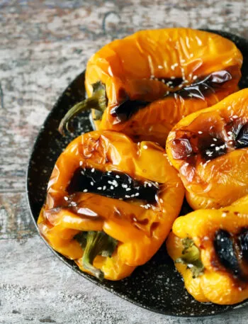 Peperoni gialli e arancioni arrostiti interi con la pelle raggrinzita e abbrustolita su un piatto scuro