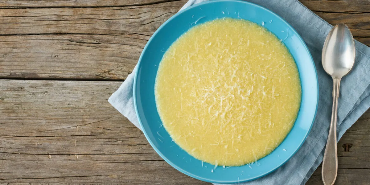 Piatto di polenta cremosa con una spolverata di Parmigiano grattugiato e un cucchiaio accanto