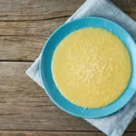 Piatto di polenta cremosa con una spolverata di Parmigiano grattugiato e un cucchiaio accanto