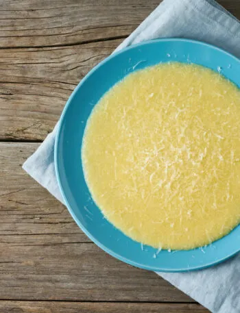 Piatto di polenta cremosa con una spolverata di Parmigiano grattugiato e un cucchiaio accanto
