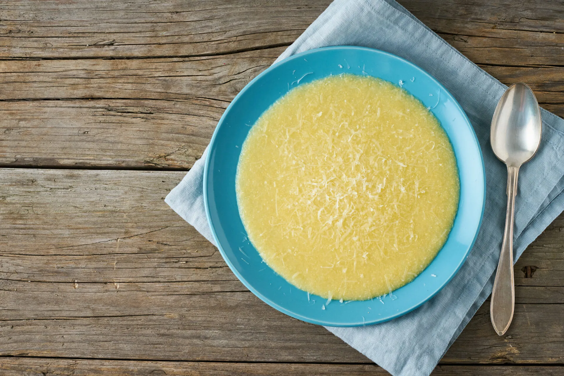 Piatto di polenta cremosa con una spolverata di Parmigiano grattugiato e un cucchiaio accanto
