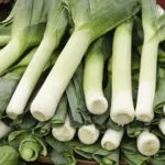 Porri freschi con fusto bianco e foglie verdi su un banco
