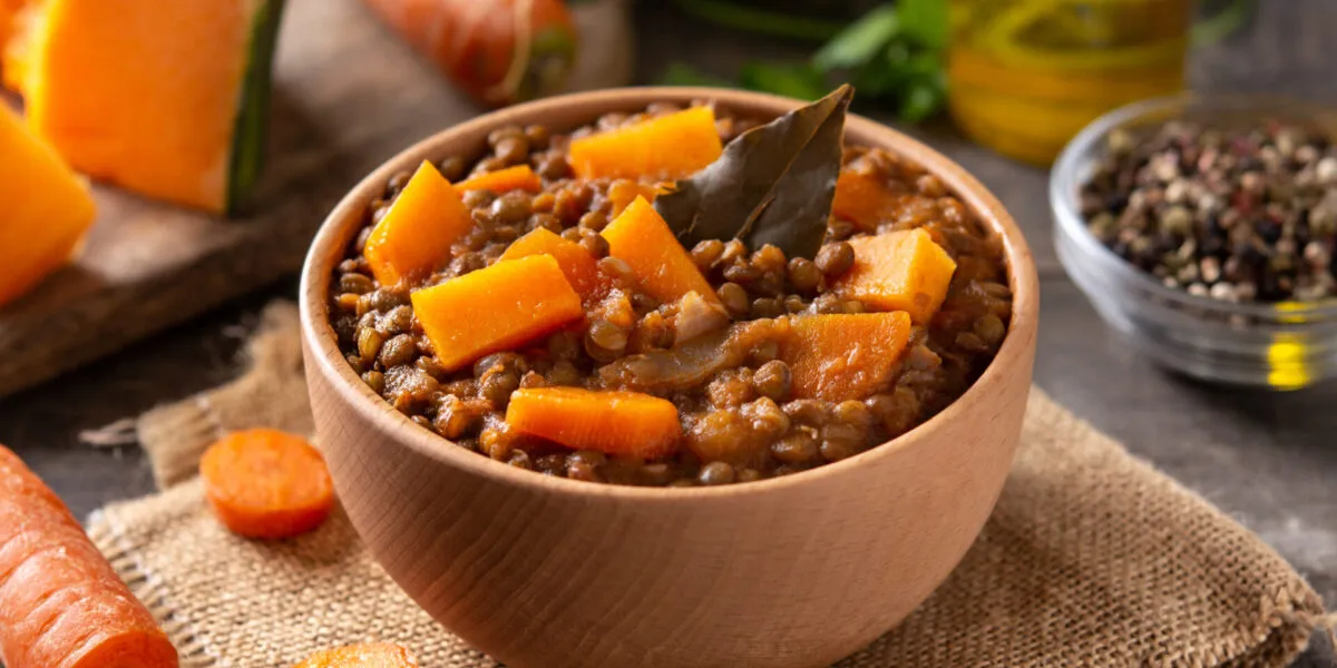 Ciotola di minestra di zucca e lenticchie con cubetti di zucca, lenticchie intere e una foglia di alloro