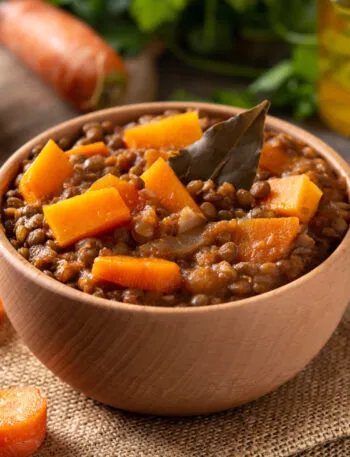 Ciotola di minestra di zucca e lenticchie con cubetti di zucca, lenticchie intere e una foglia di alloro