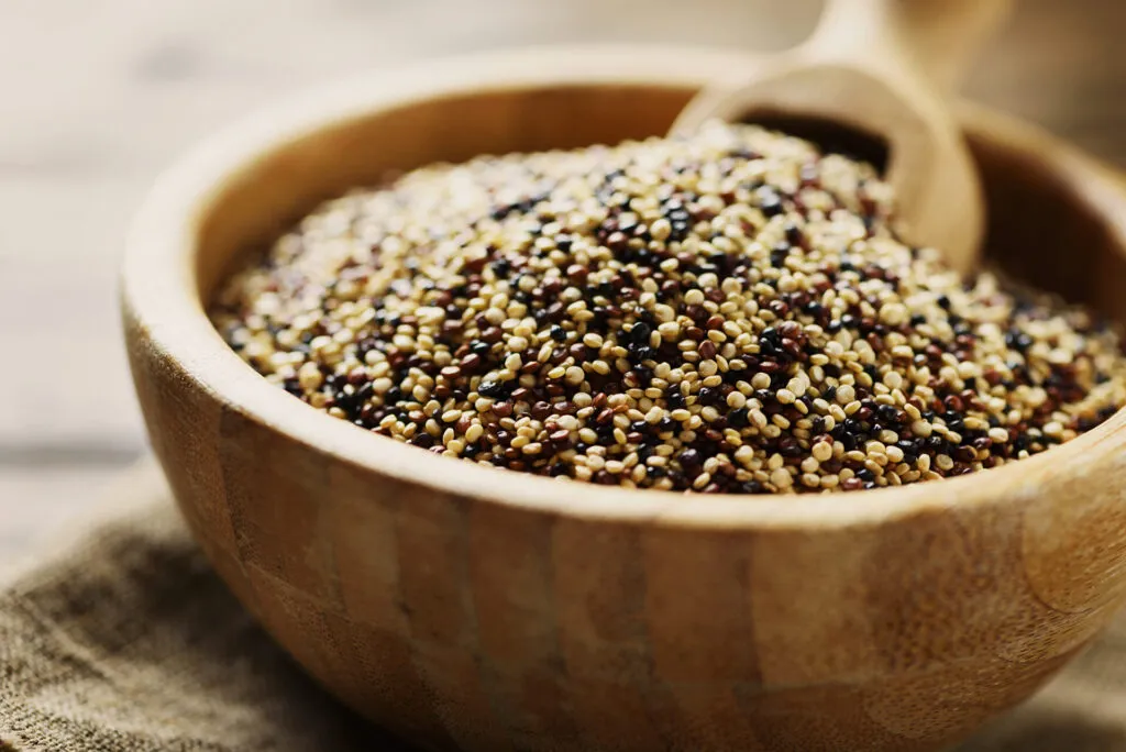 Quinoa cruda tricolore, bianca rossa e nera, in una ciotola di legno con cucchiaio di legno
