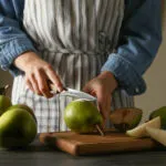 Donna con grembiule che taglia una pera su un tagliere di legno, con altre pere intere e a spicchi accanto