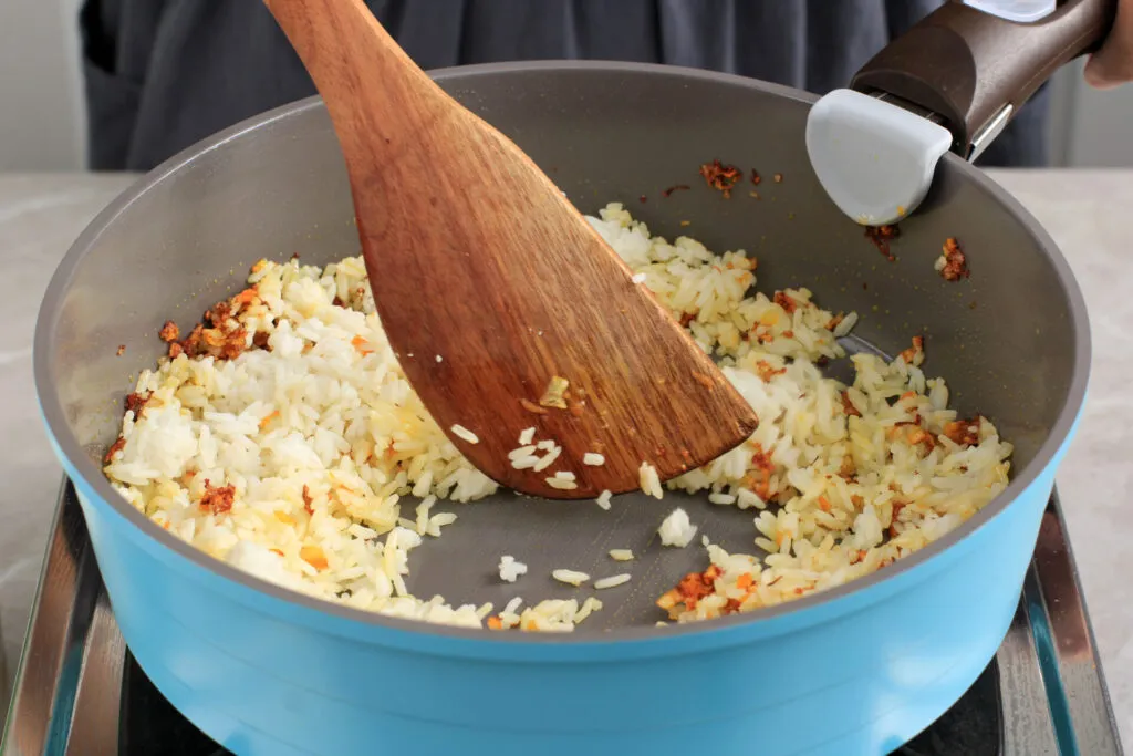 Riso cotto sgranato ripassato in padella con una spatola di legno, con qualche pezzetto dorato di soffritto sul fondo