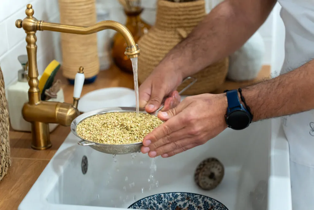 Semi sciacquati in un colino a maglia fine sotto l'acqua corrente, tenuto con entrambe le mani sopra il lavello