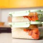 Due contenitori di vetro impilati con coperchio a scatto, riempiti con riso bianco, carote e verdure, appoggiati sul piano della cucina