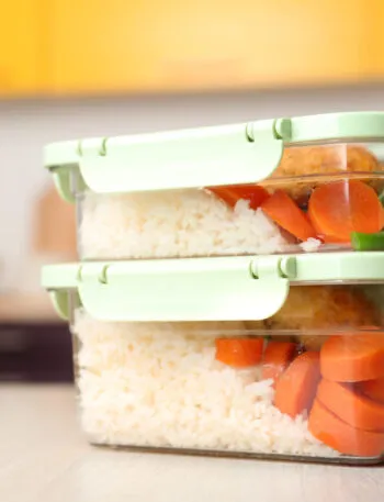 Due contenitori di vetro impilati con coperchio a scatto, riempiti con riso bianco, carote e verdure, appoggiati sul piano della cucina