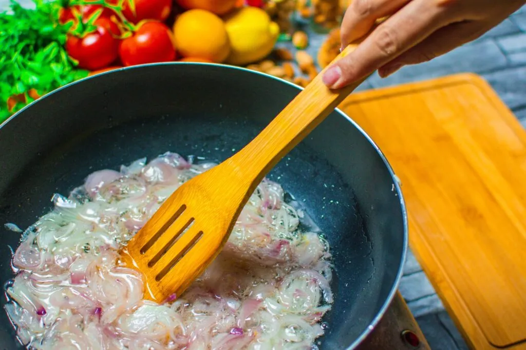 Cipolla affettata che stufa in padella nella sua acqua di vegetazione, mescolata con una spatola di legno, ancora traslucida e senza doratura