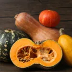 Diverse varietà di zucca a confronto, tonde e allungate, con una tagliata a metà che mostra la polpa arancione e i semi