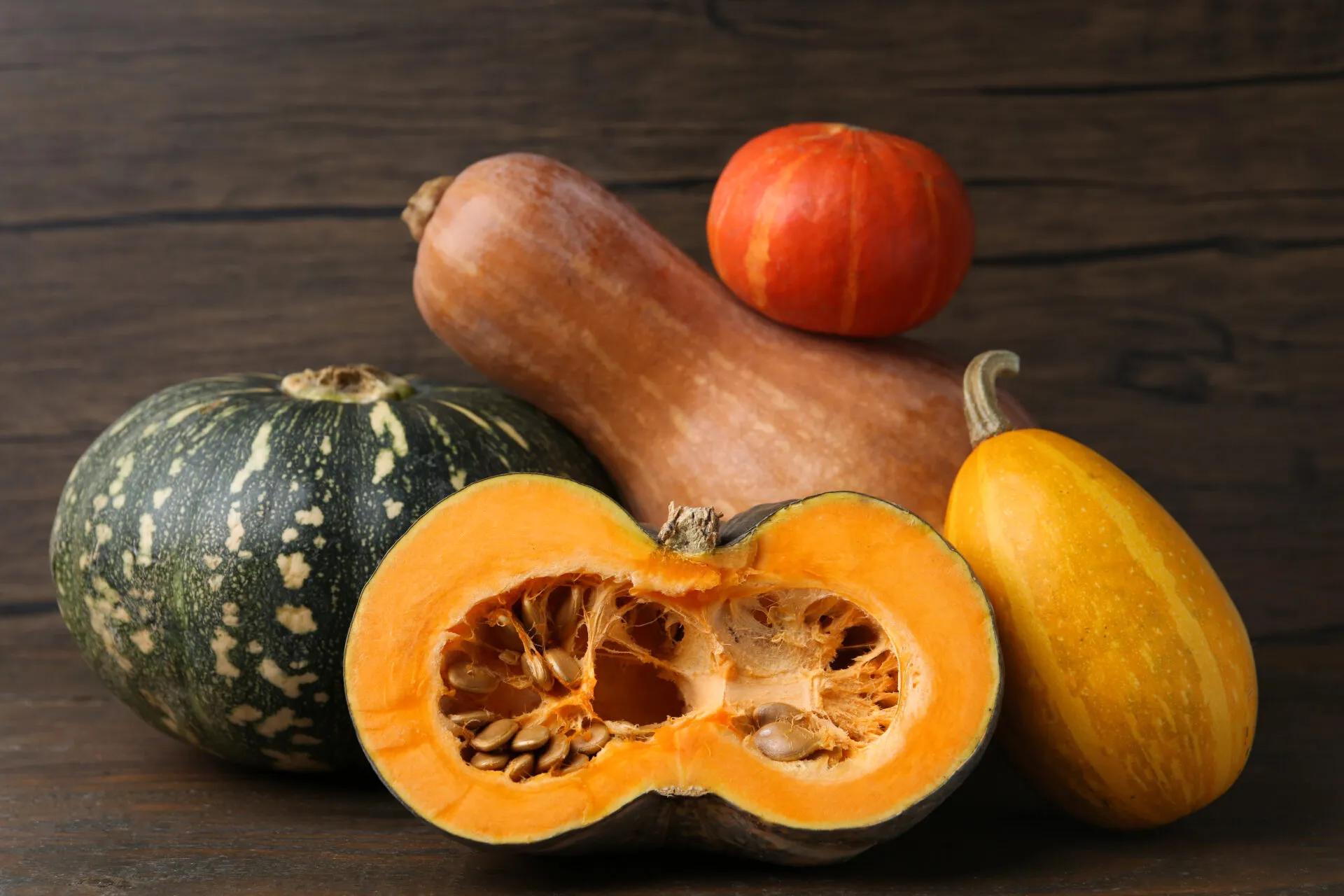 Diverse varietà di zucca a confronto, tonde e allungate, con una tagliata a metà che mostra la polpa arancione e i semi