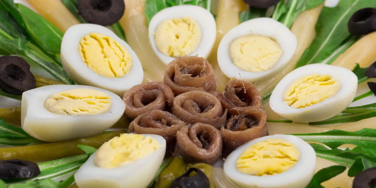 Uova sode tagliate a metà in un'insalata con acciughe e olive